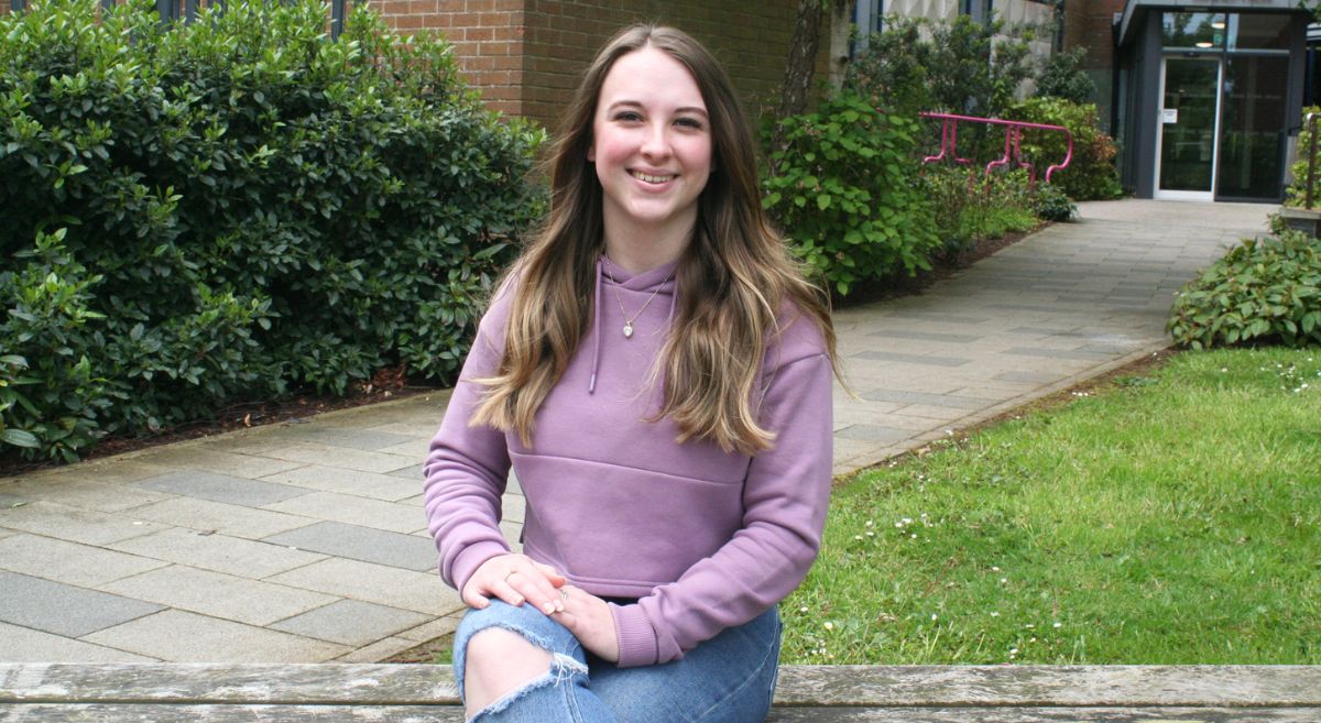 Amy Brown pictured sitting on a bench in front of the Bangor campus. 